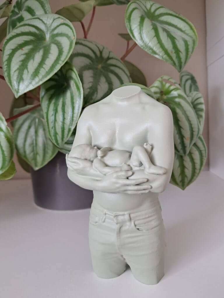 3D-ouder-en-babybeeldje waarbij een vader zijn liggende baby met beide handen ondersteunt, met groene bladeren op de achtergrond.